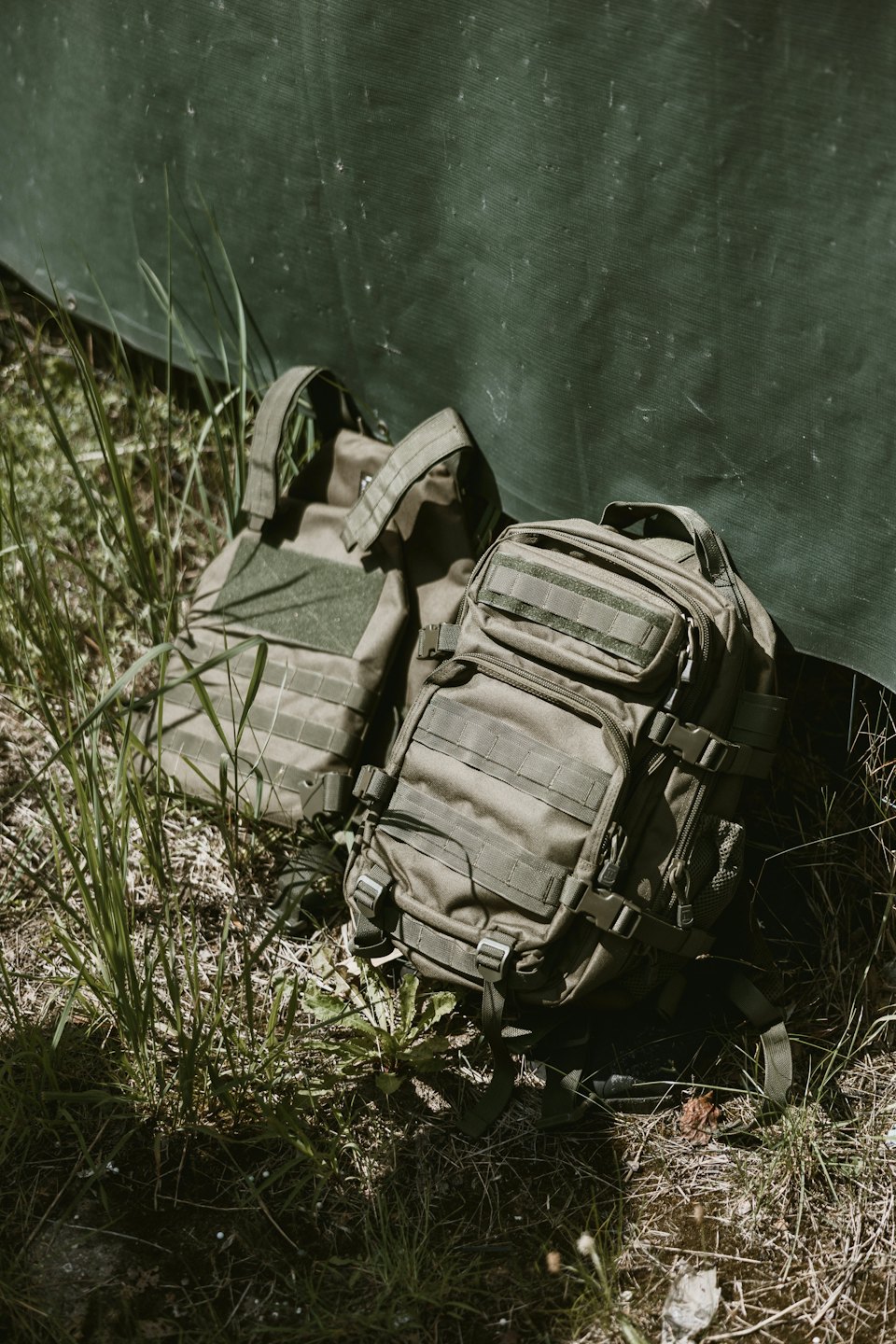 Tactical backpack and vest resting against a canvas tarp.