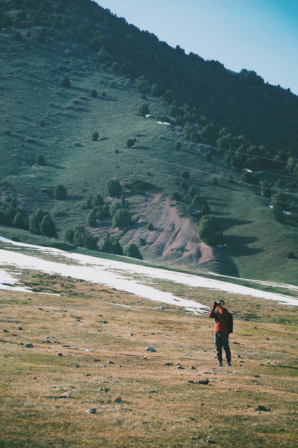 Hiker in a red top uses binoculars to view mountains.