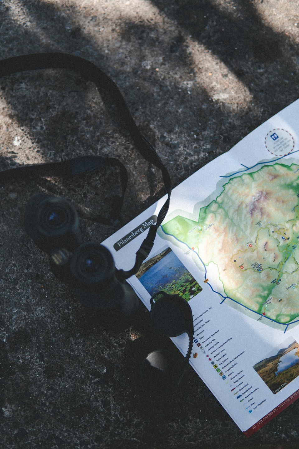 Binoculars and Pilanesberg map on a rocky surface.